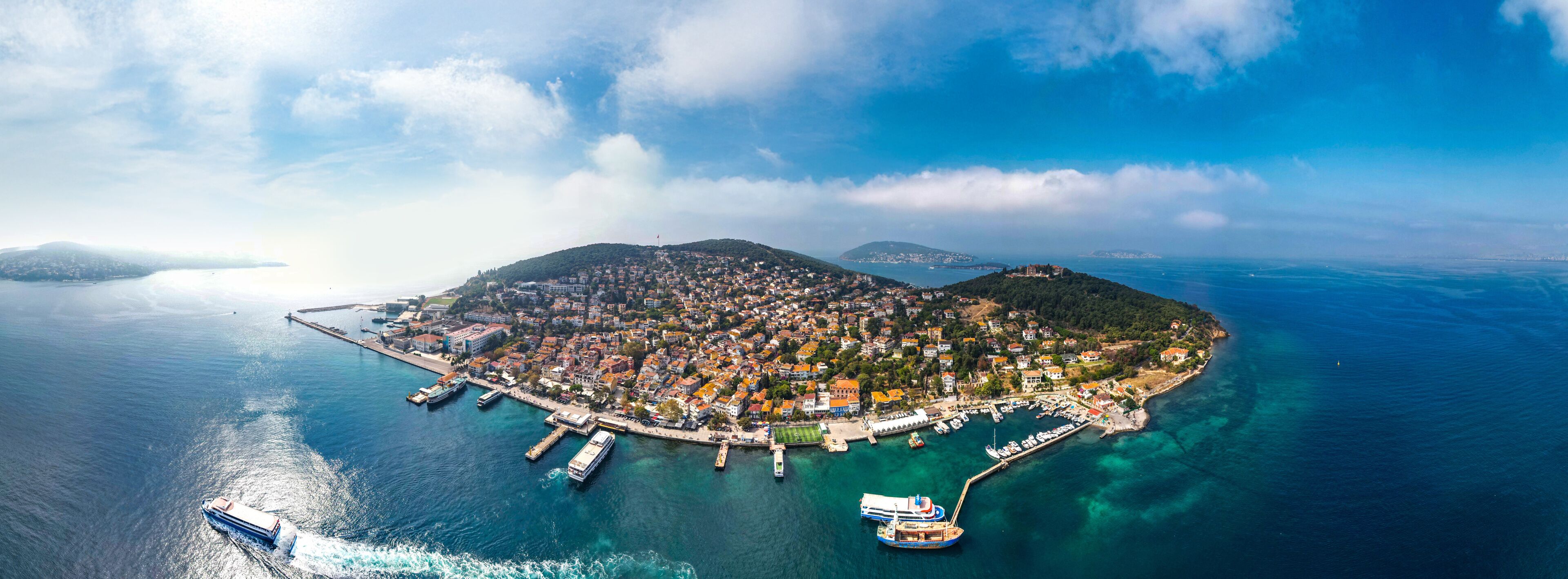An aerial view of a coastal town with a harbor, boats, and a mountainous backdrop.