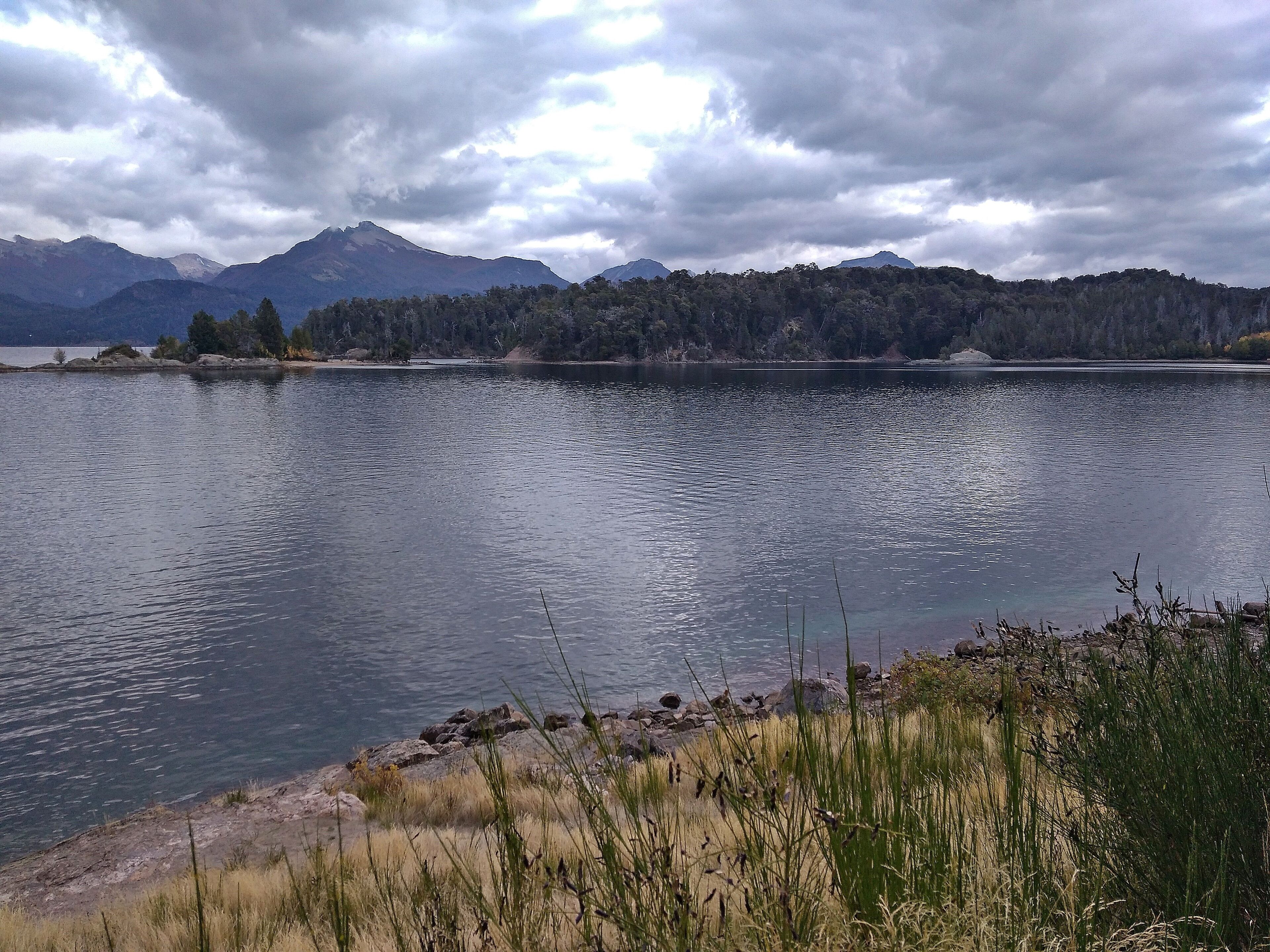 A calm lake with mountains in the background and grassy areas in the foreground.