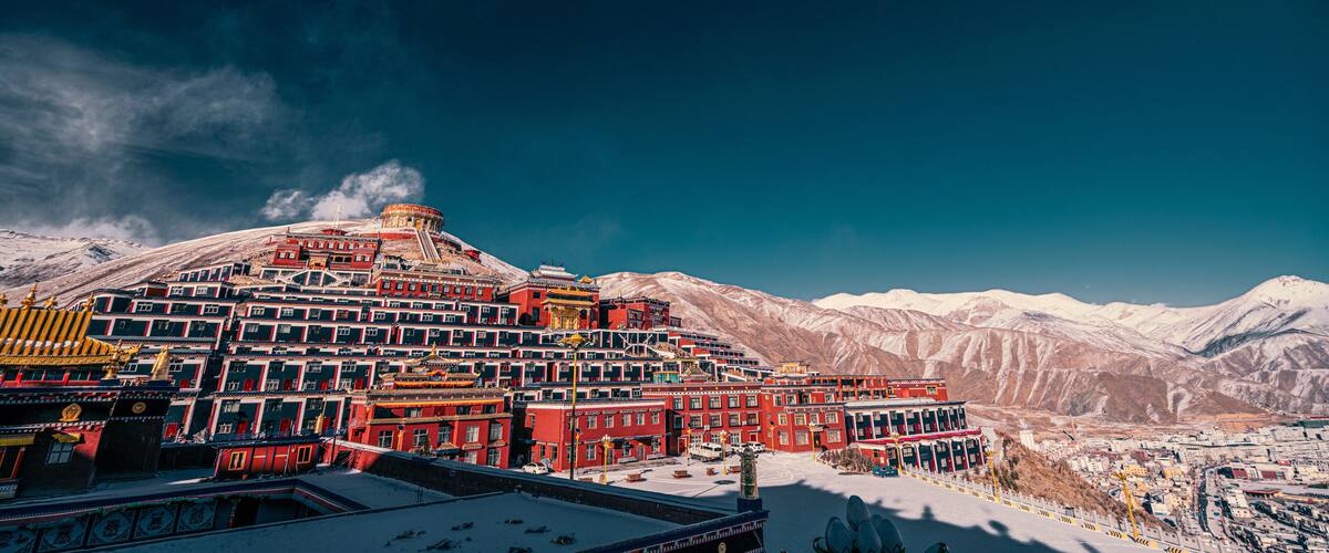 A snow-covered mountain range with a traditional red-roofed building complex.