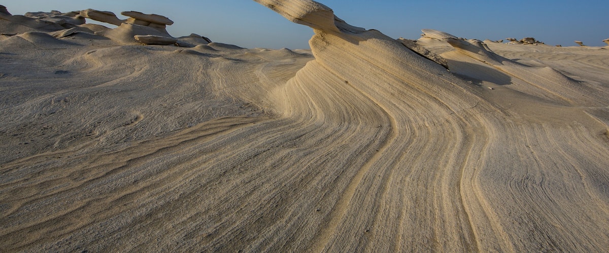 A desert landscape with prominent sand formations and a clear blue sky.