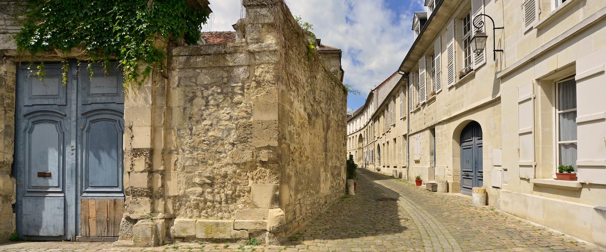 A cobblestone street flanked by historic buildings with stone walls and blue doors.