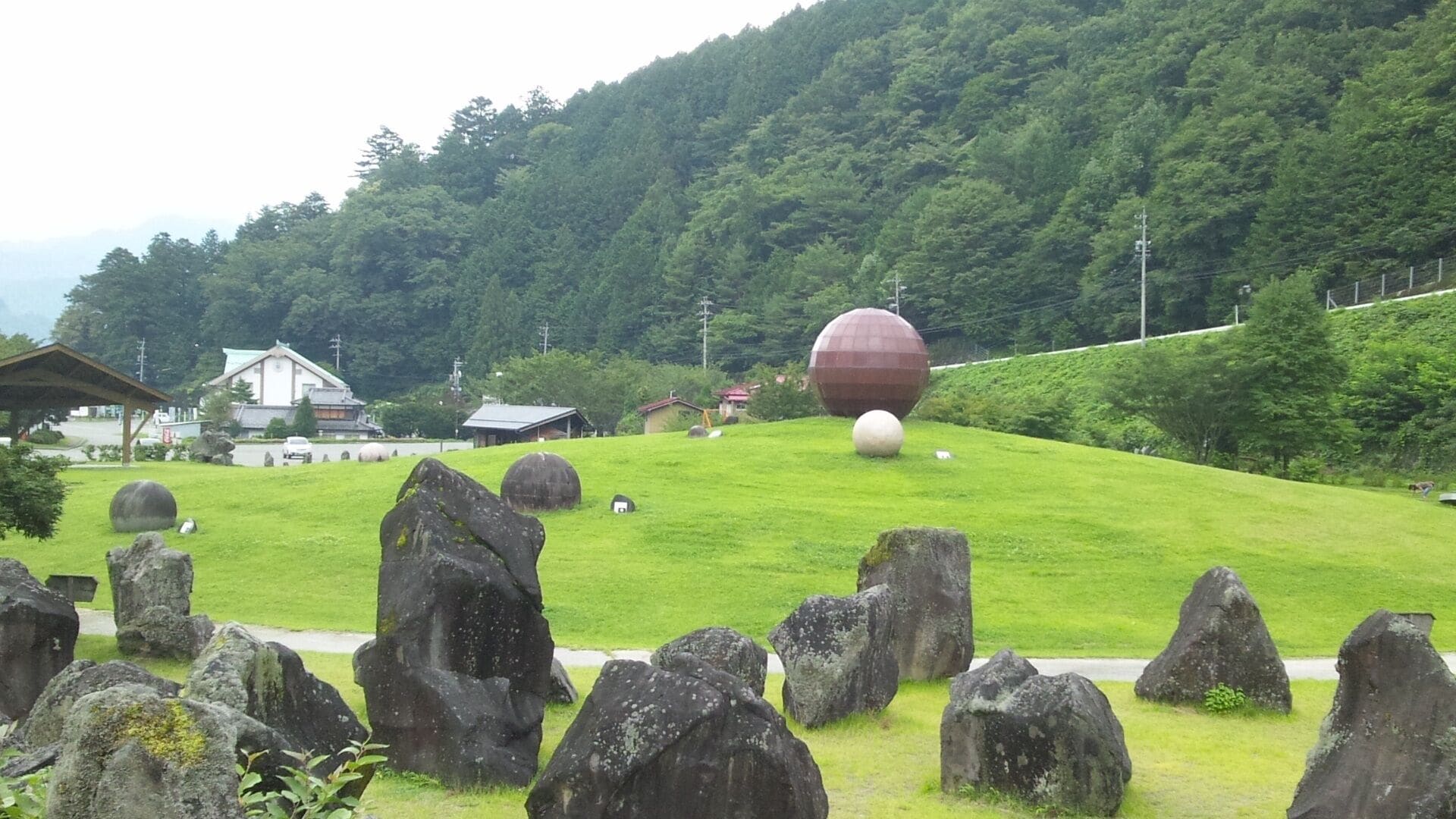 Uma colina gramada com pedras esféricas grandes e um edifício ao fundo.