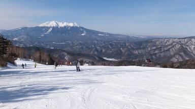 A snowy ski slope with skiers, a mountain in the background, and a clear sky.