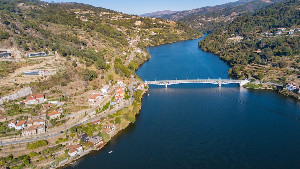 A river with a bridge, surrounded by hills and houses.