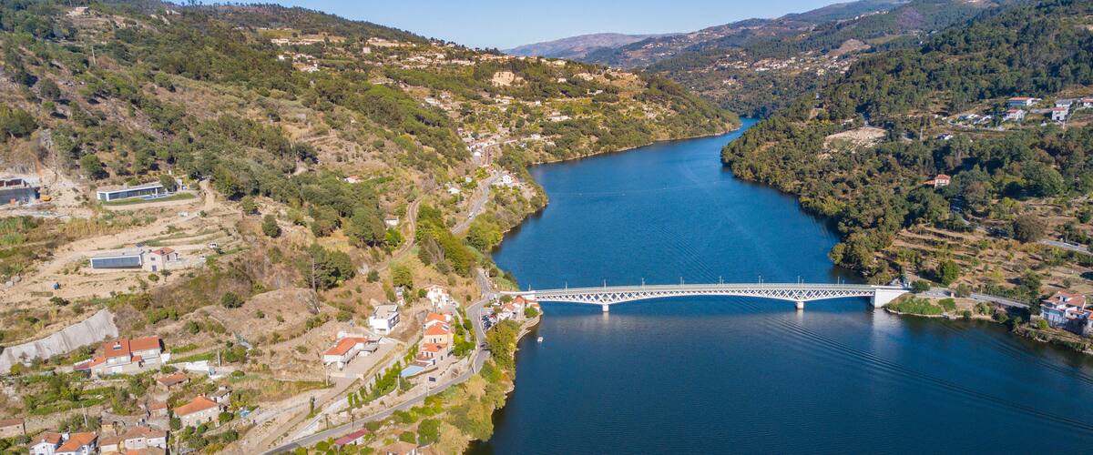 A river with a bridge, surrounded by hills and houses.