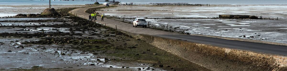 A coastal road with a white car, a pedestrian path, and a distant shoreline.
