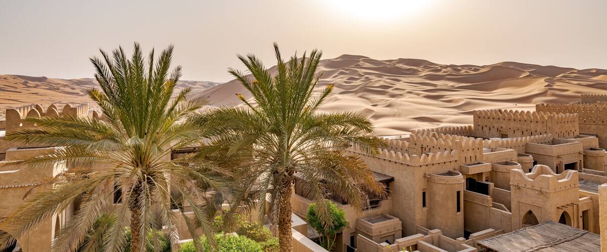 A desert landscape with palm trees and traditional architecture.
