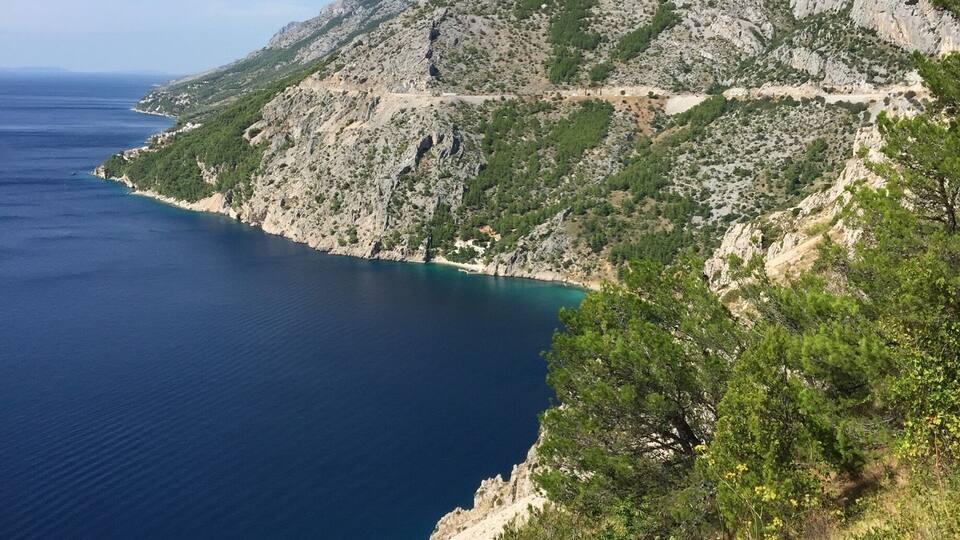 A coastal mountain landscape with a clear blue sea and rocky terrain.