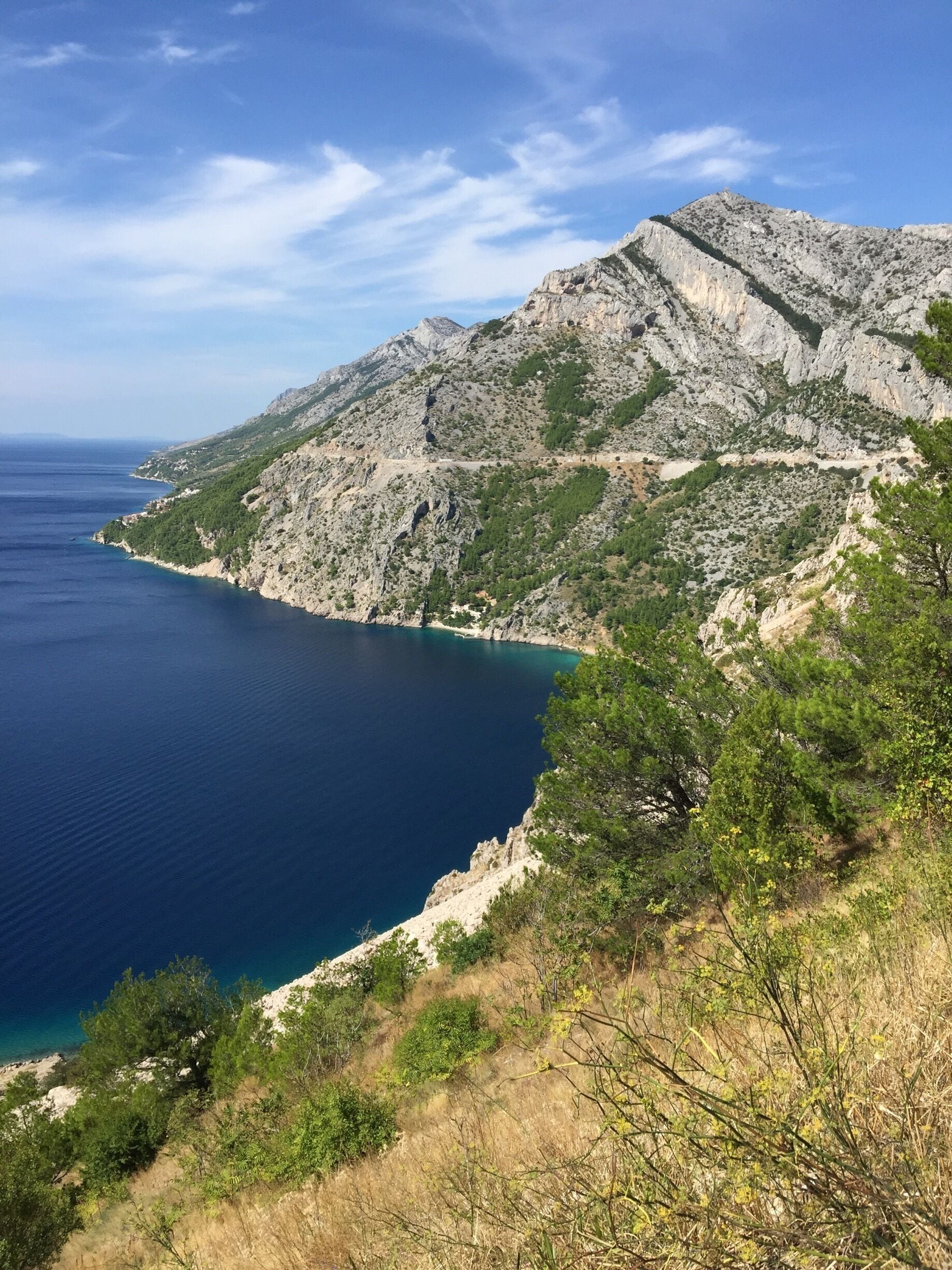 A coastal mountain landscape with a clear blue sea and rocky terrain.