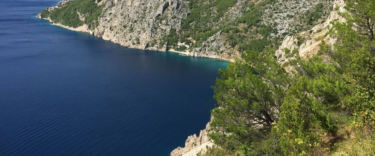 A coastal mountain landscape with a clear blue sea and rocky terrain.