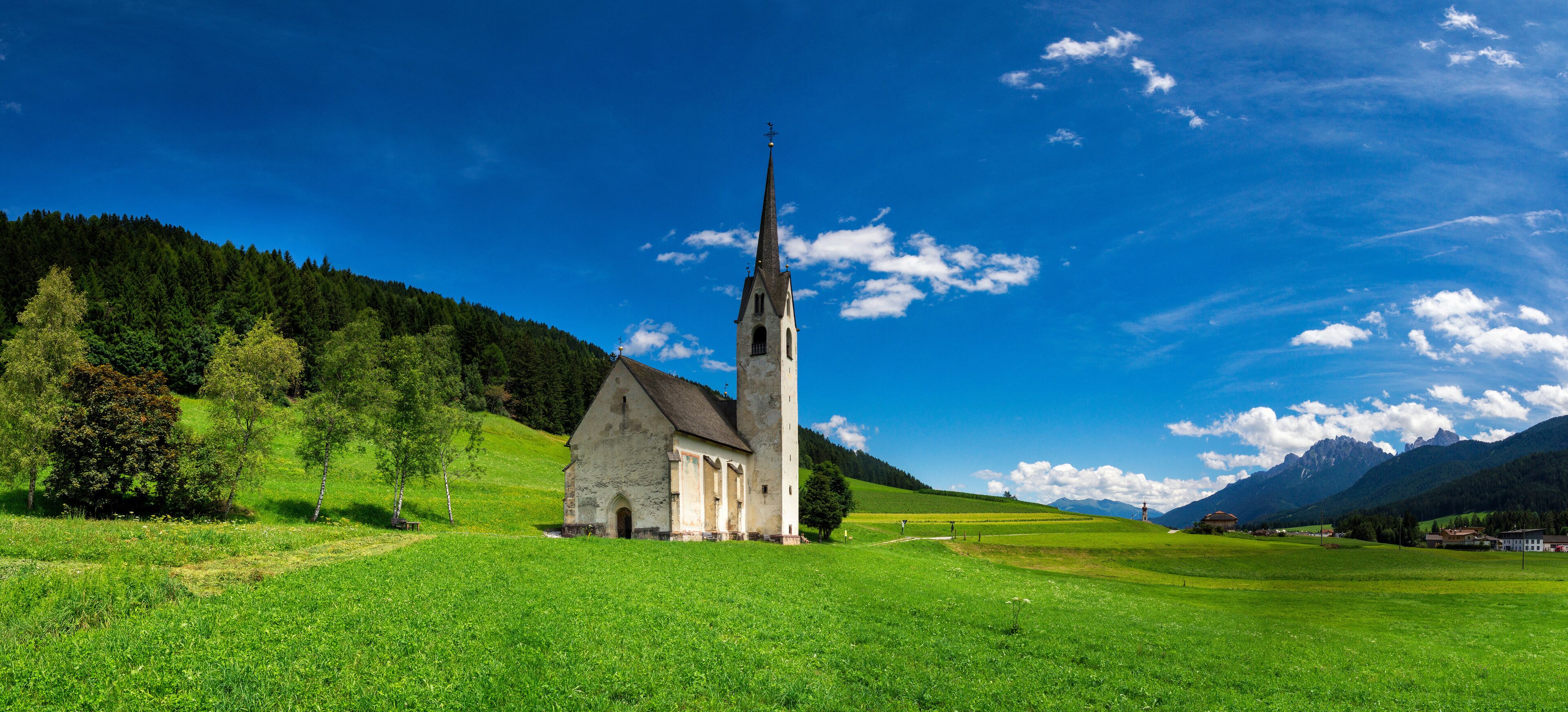 A church with a tall steeple surrounded by lush green fields and mountains in the background.