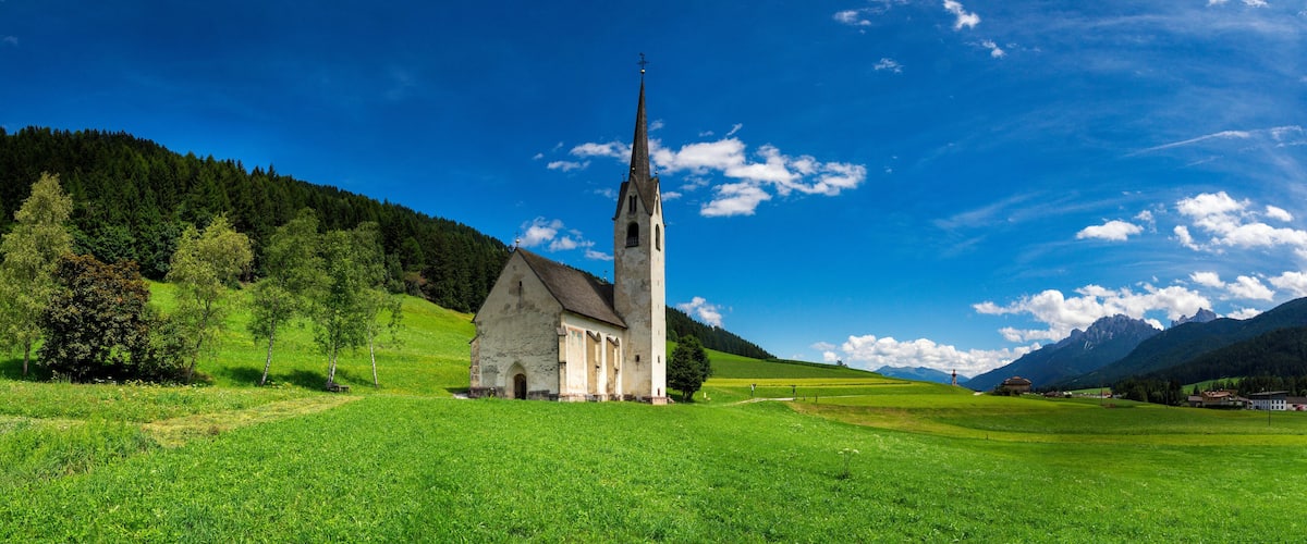 A church with a tall steeple surrounded by lush green fields and mountains in the background.