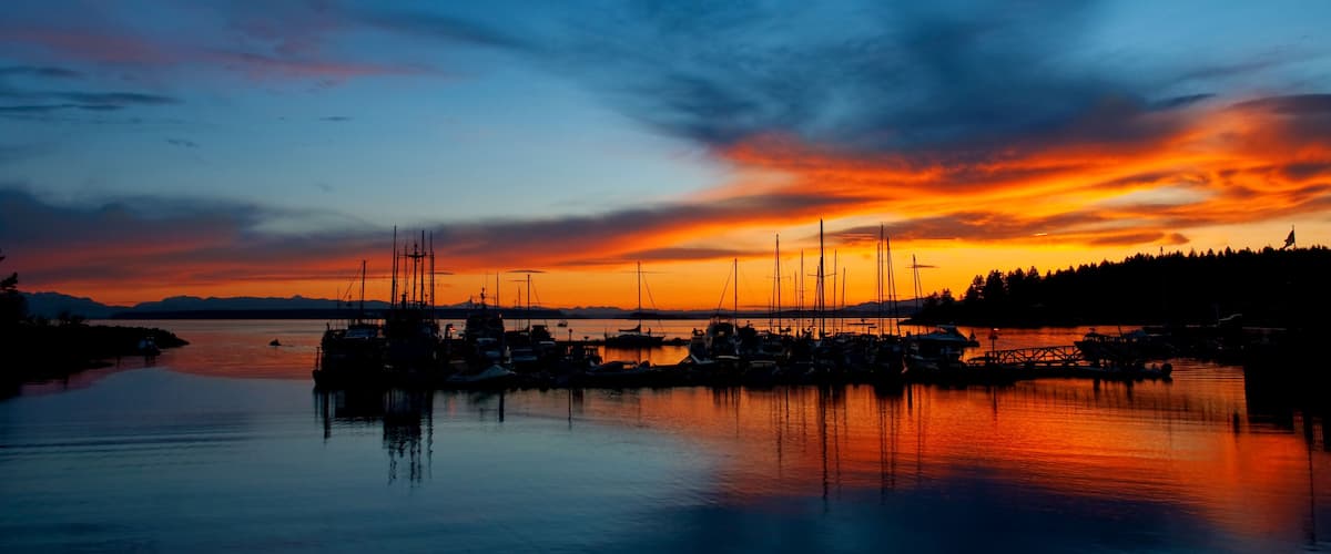 A sunset over a harbor with boats and a flag.
