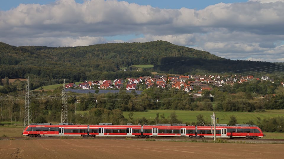 A red train on tracks with a town and hills in the background.