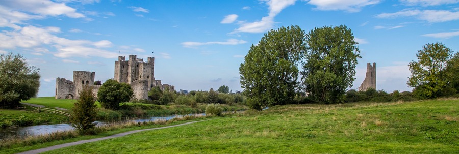 A historic castle with ruins, a river, and a pathway.