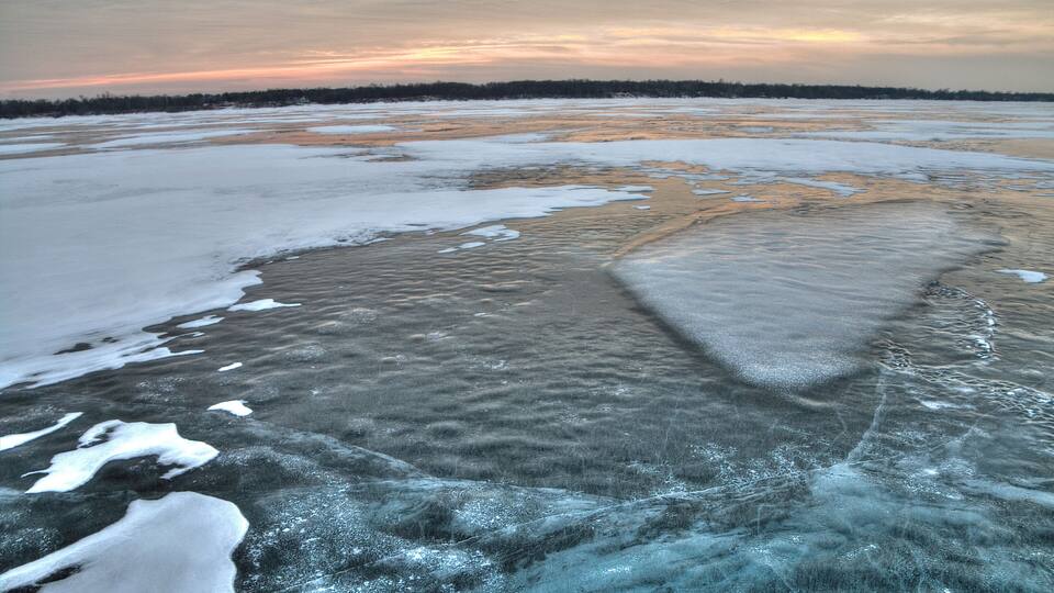 A frozen landscape with ice patches and a distant forest line.