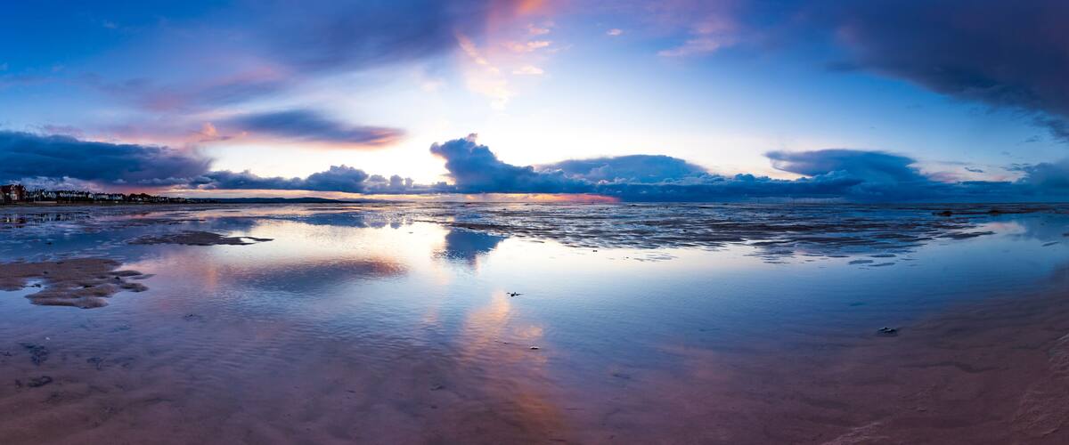 A beach with a calm sea reflecting the sky.