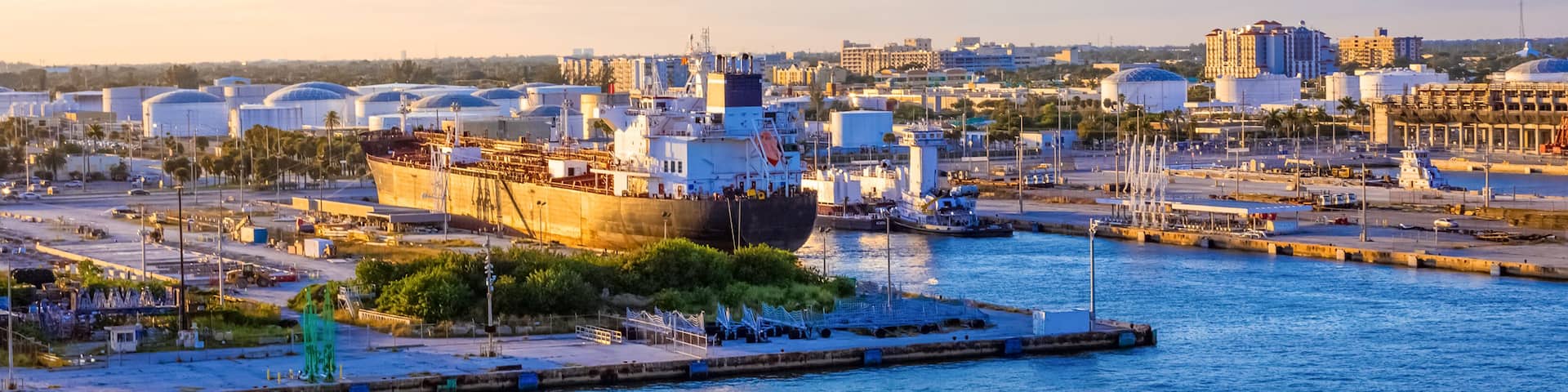 A harbor with a large ship docked, industrial buildings, and a clear sky.