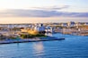 A harbor with a large ship docked, industrial buildings, and a clear sky.