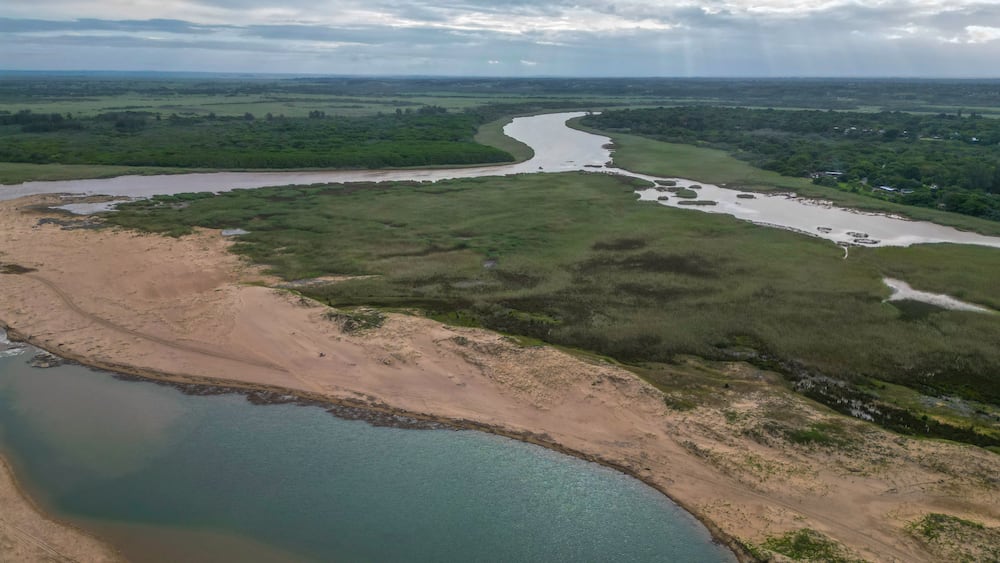 Une rivière serpente à travers un paysage verdoyant, bordée d’une plage de sable.