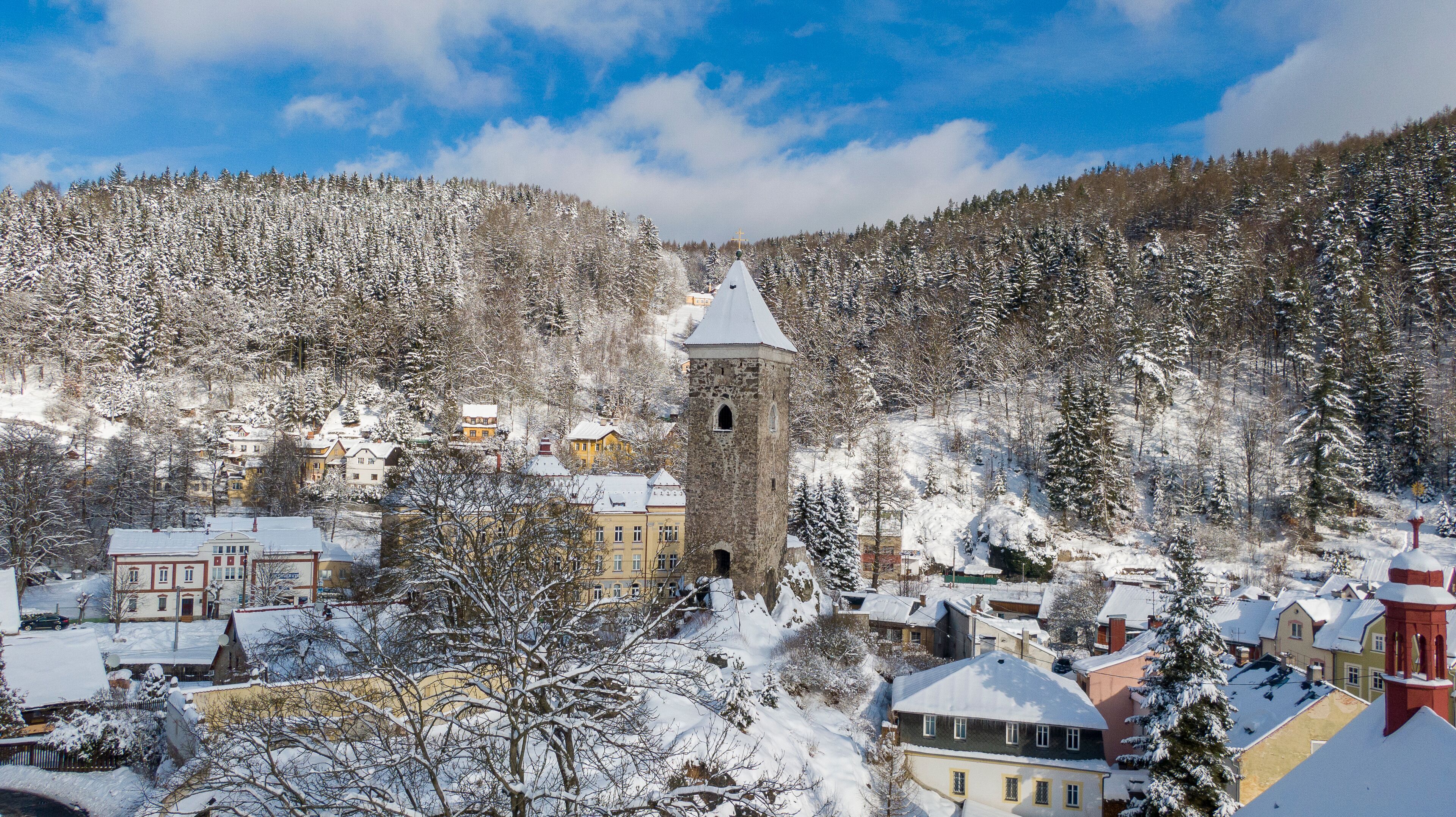 A snow-covered town with a prominent tower and surrounding forest.
