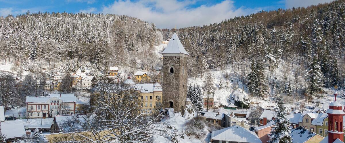 A snow-covered town with a prominent tower and surrounding forest.