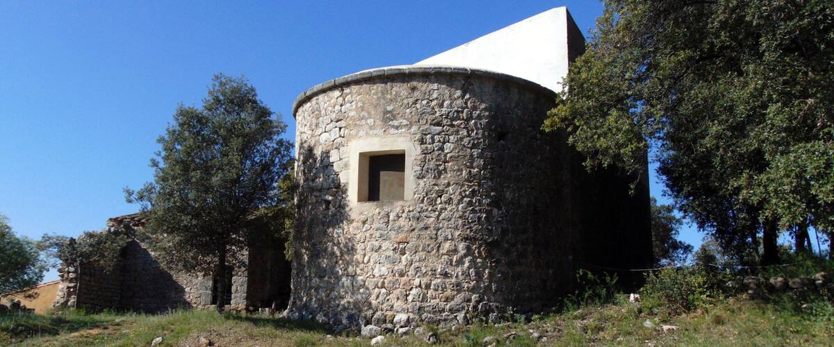 A stone tower with a small window, surrounded by trees and grass.