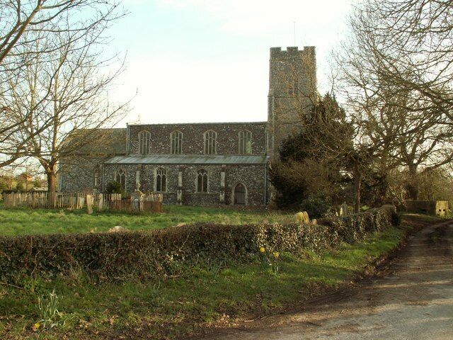 A church with a tower and arched windows, surrounded by a hedge and a rural road.