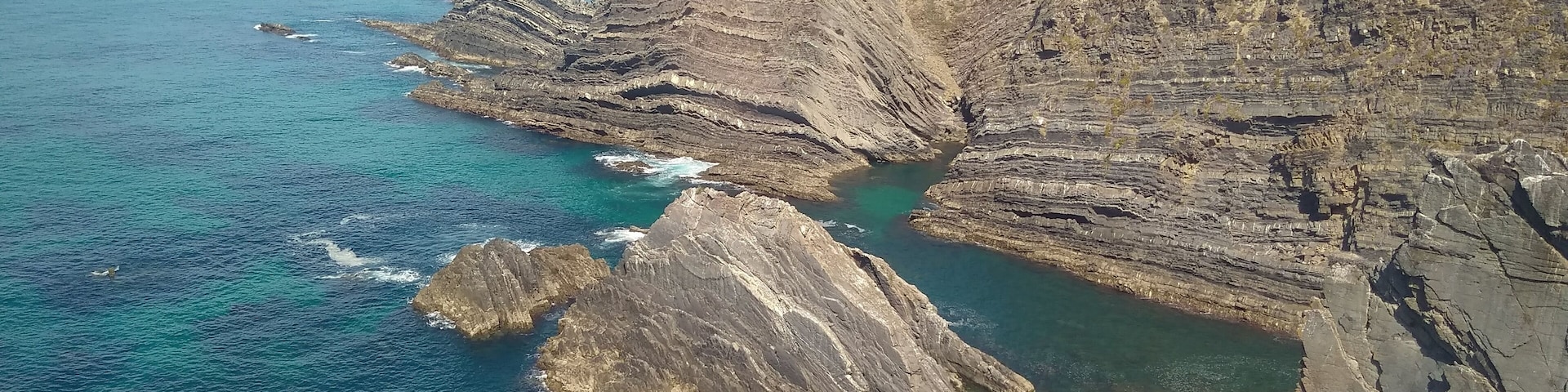 A coastal cliff with layered rock formations and clear blue waters.