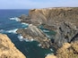 A coastal cliff with layered rock formations and a clear blue sea.