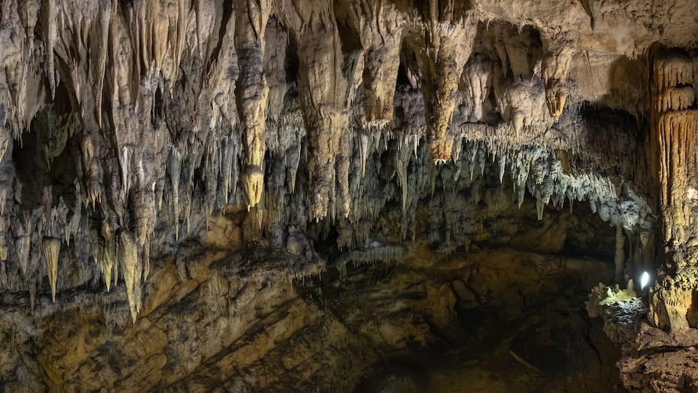 Une grotte ornée de stalactites pendant du plafond et de stalagmites s’élevant du sol.