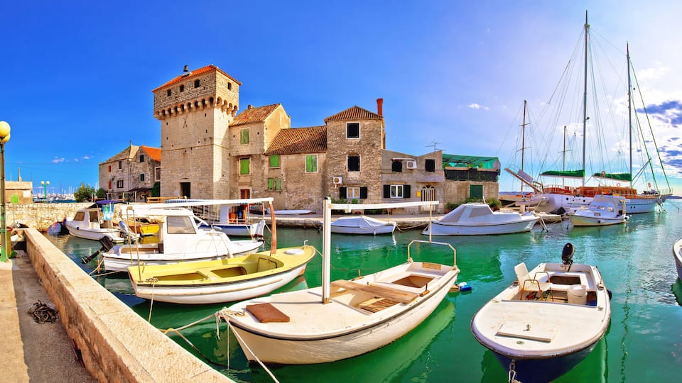 A harbor with boats, a historic stone building, and a sailboat.