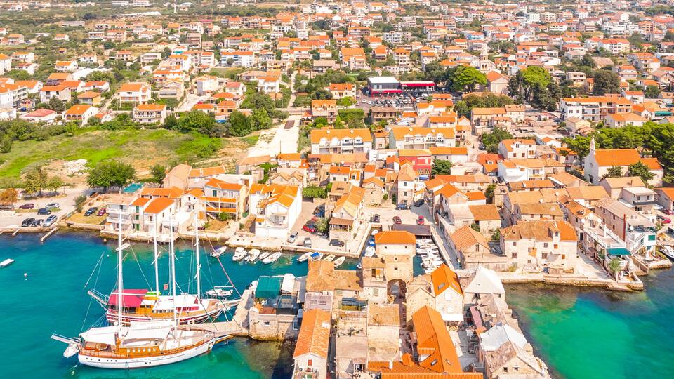 An aerial view of a coastal town with a harbor, boats, and a prominent castle-like structure.