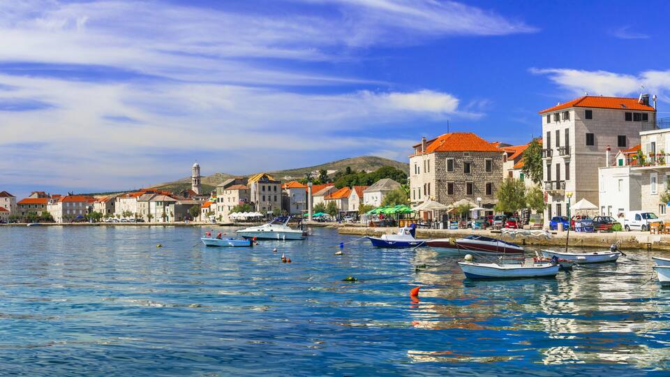 A coastal town with historic buildings, a clear blue sky, and calm waters with small boats.