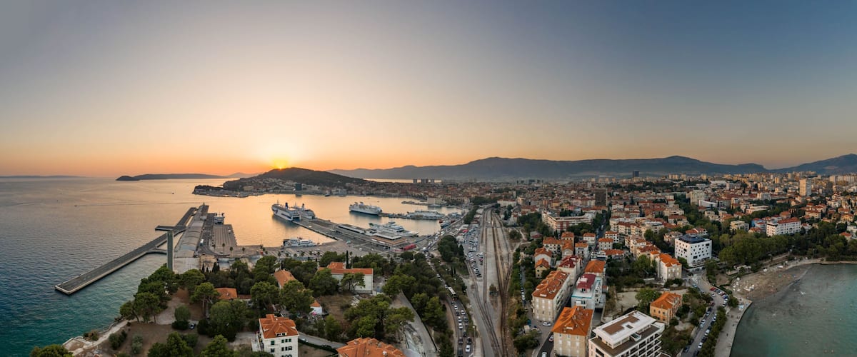 A coastal cityscape with a prominent port, a bridge, and a sunset over the sea.