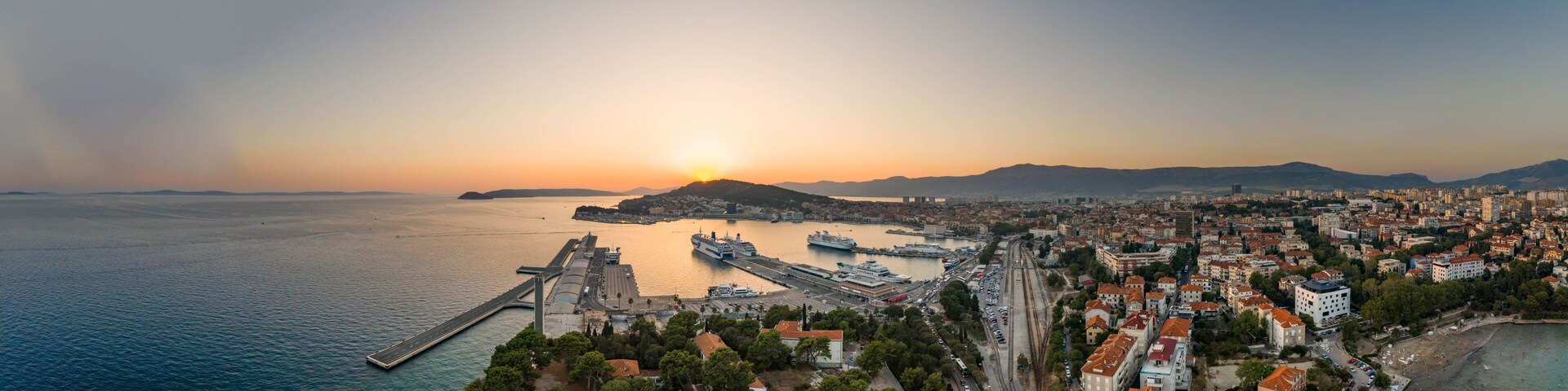 A coastal cityscape with a prominent port, a bridge, and a sunset over the sea.