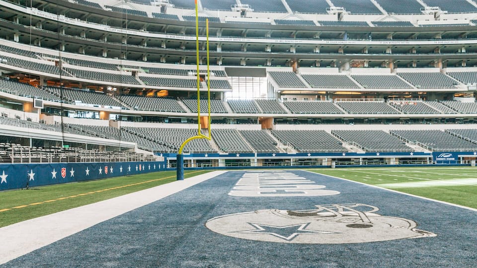 An empty stadium with a football field and a large "Cowboys Stadium" sign.