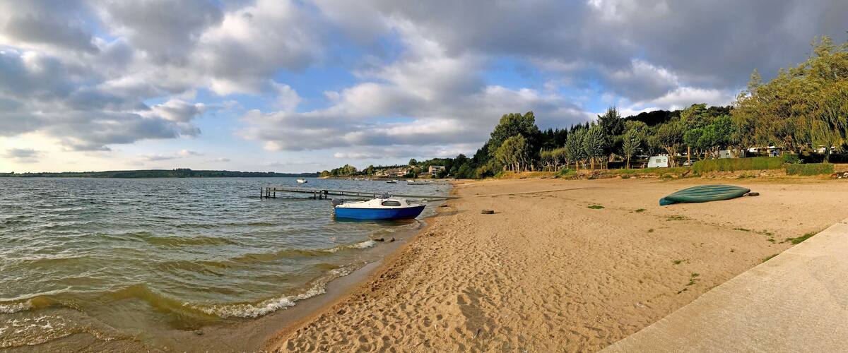 A sandy beach with a blue boat docked on the shore, a concrete path, and a row of houses in the background.