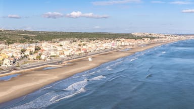 Uma cidade costeira com uma extensa praia, edifícios e uma paisagem montanhosa ao fundo.