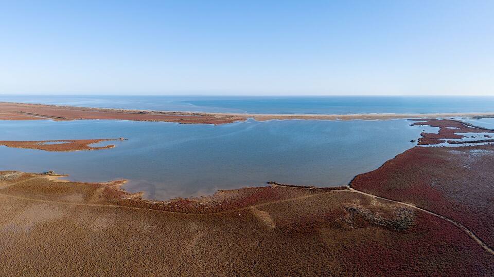 An aerial view of a coastal landscape with a large body of water, sandy areas, and a distant shoreline.