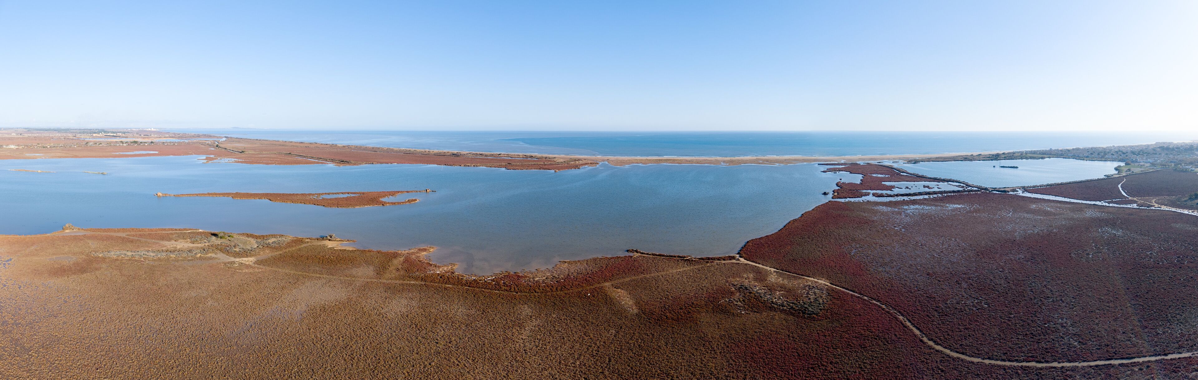 An aerial view of a coastal landscape with a large body of water, sandy areas, and a distant shoreline.