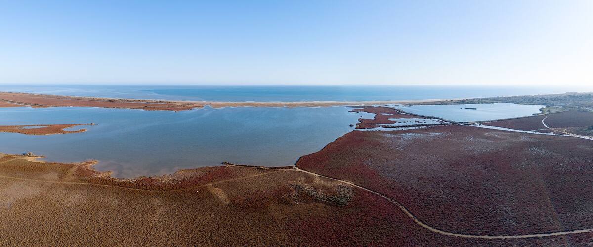 An aerial view of a coastal landscape with a large body of water, sandy areas, and a distant shoreline.