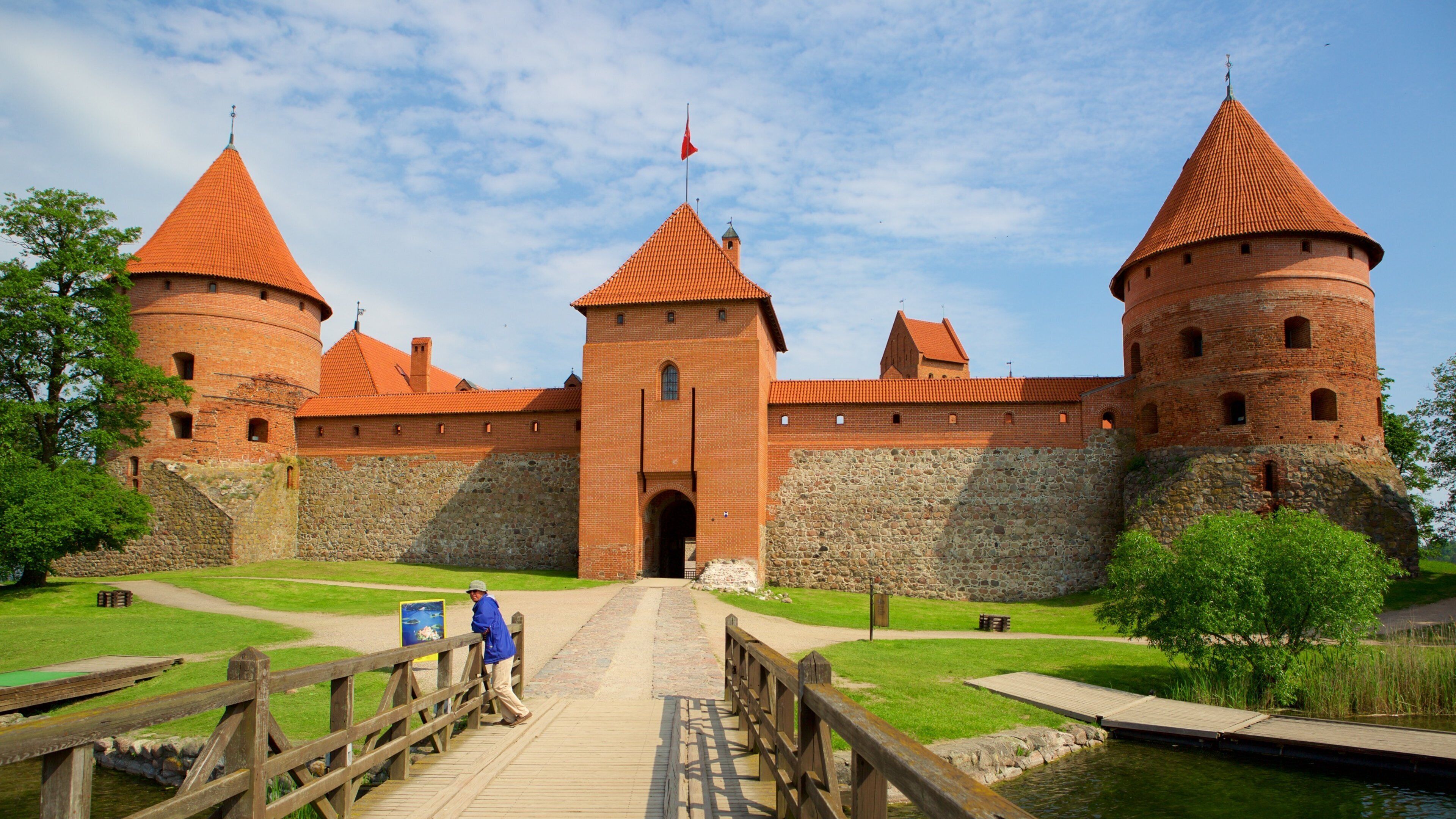 A historic brick castle with red-tiled roofs and a wooden bridge leading to the entrance.