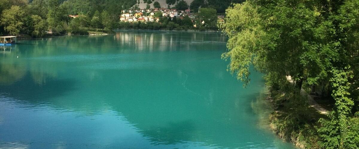 A turquoise lake surrounded by lush green hills and a small village.
