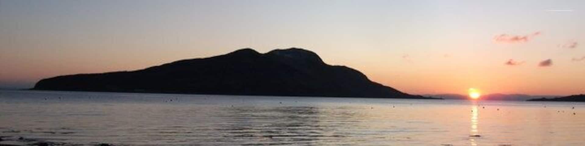 A sunset over a calm sea with a silhouette of a mountain in the distance.