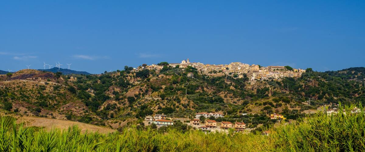 A coastal town with wind turbines on a hill, surrounded by greenery and buildings.
