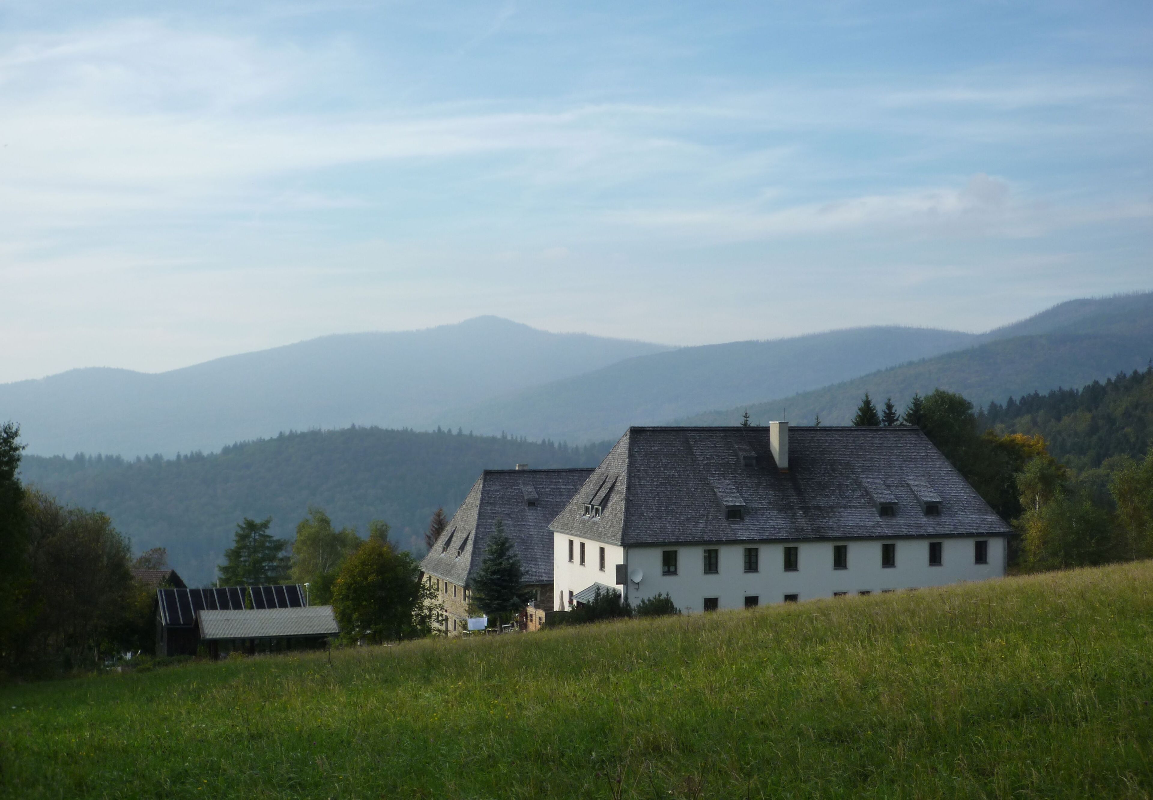 A rural landscape with two white houses on a hill, surrounded by green fields and mountains in the background.