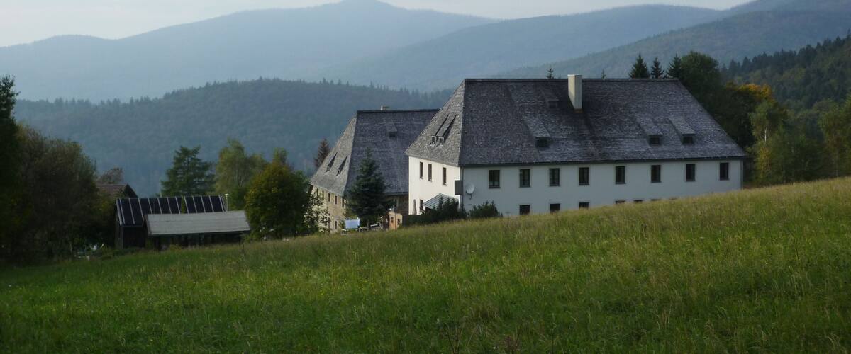 A rural landscape with two white houses on a hill, surrounded by green fields and mountains in the background.