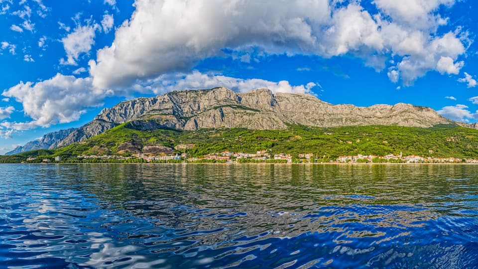 A mountainous island with a village, surrounded by a calm sea under a partly cloudy sky.