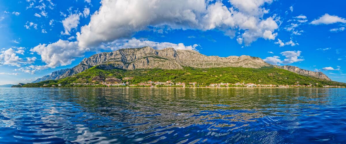 A mountainous island with a village, surrounded by a calm sea under a partly cloudy sky.